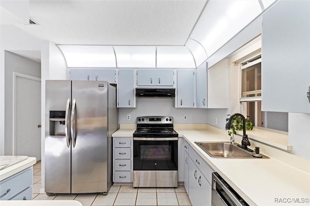 kitchen with light countertops, under cabinet range hood, a sink, appliances with stainless steel finishes, and light tile patterned floors