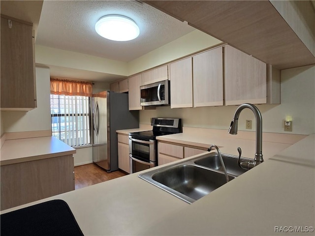 kitchen featuring stainless steel appliances, sink, a textured ceiling, and light wood-type flooring