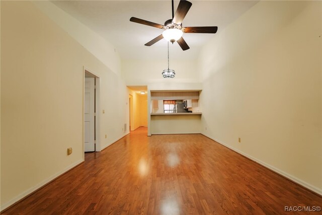 unfurnished living room featuring ceiling fan, hardwood / wood-style floors, and a towering ceiling