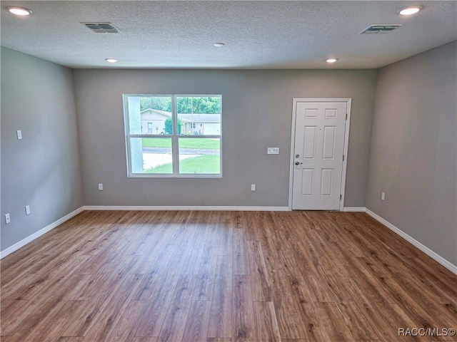 spare room with visible vents, a textured ceiling, baseboards, and wood finished floors