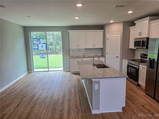 kitchen featuring stainless steel appliances, wood finished floors, a sink, white cabinets, and tasteful backsplash