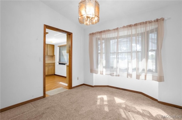 carpeted empty room with an inviting chandelier and lofted ceiling