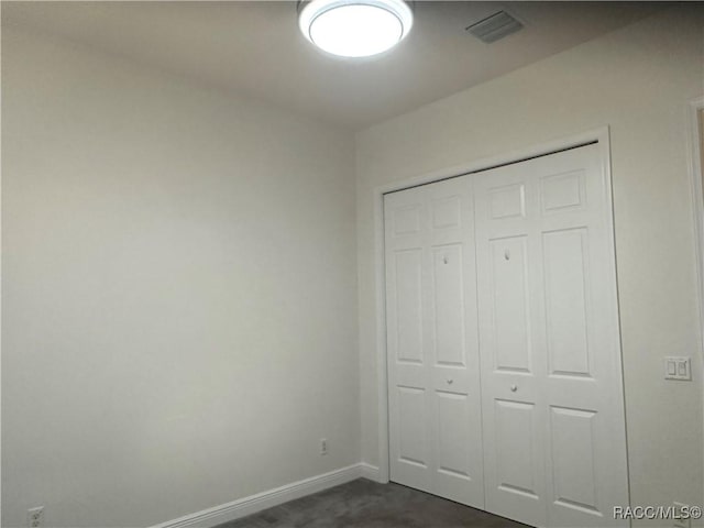 unfurnished bedroom with a closet, visible vents, dark carpet, and baseboards