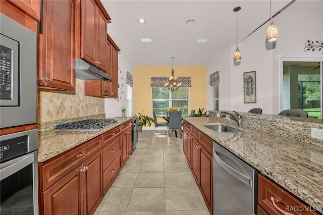 kitchen with light stone counters, a sink, stainless steel appliances, under cabinet range hood, and backsplash