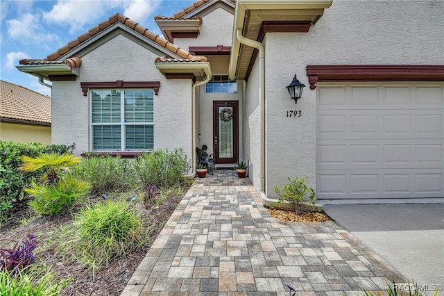 property entrance featuring a garage, a tile roof, and stucco siding