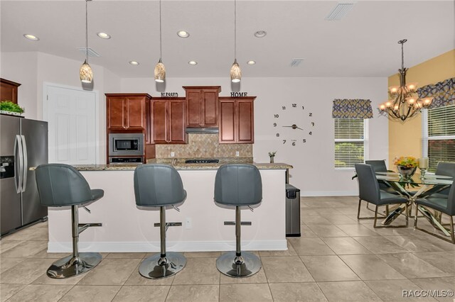 kitchen with sink, light stone counters, decorative light fixtures, a kitchen island with sink, and appliances with stainless steel finishes