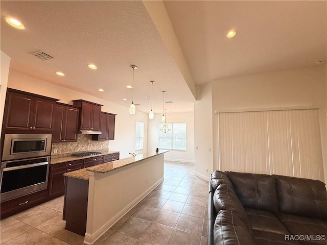 kitchen with dark brown cabinetry, tasteful backsplash, open floor plan, light stone countertops, and stainless steel appliances