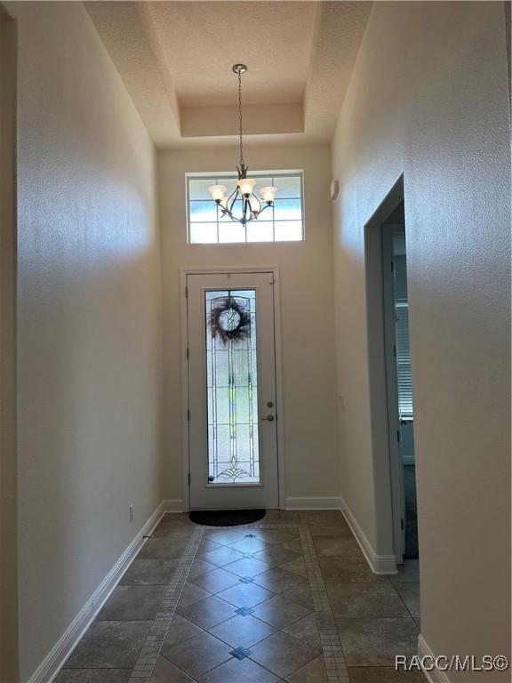 entrance foyer featuring a chandelier, a raised ceiling, a towering ceiling, and baseboards