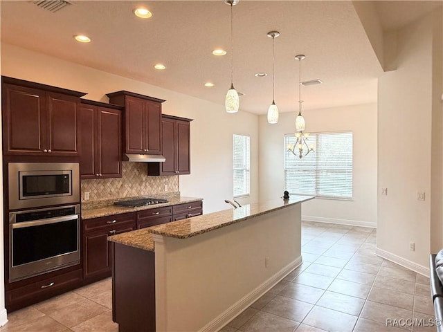 kitchen with decorative backsplash, light stone counters, hanging light fixtures, stainless steel appliances, and dark brown cabinets