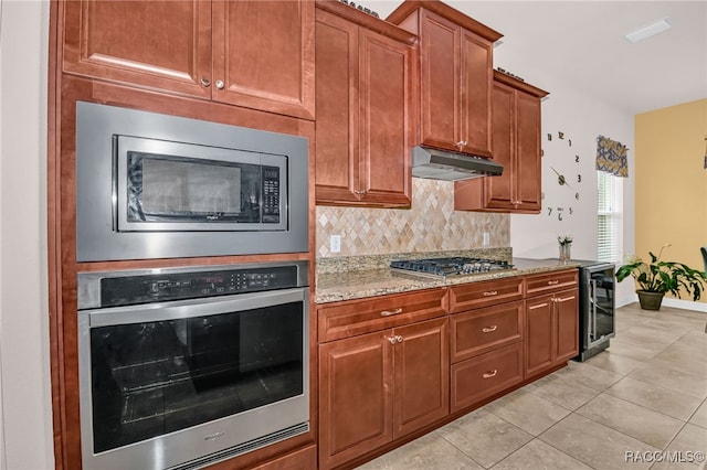 kitchen featuring appliances with stainless steel finishes, light stone counters, under cabinet range hood, backsplash, and light tile patterned flooring