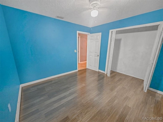 unfurnished bedroom with ceiling fan, a closet, hardwood / wood-style floors, and a textured ceiling