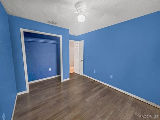 unfurnished bedroom featuring a textured ceiling, ceiling fan, dark wood-type flooring, and a closet