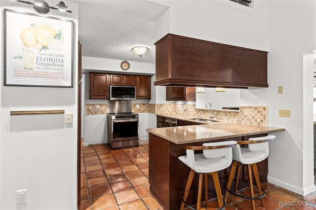 kitchen featuring kitchen peninsula, stainless steel appliances, decorative backsplash, a textured ceiling, and sink