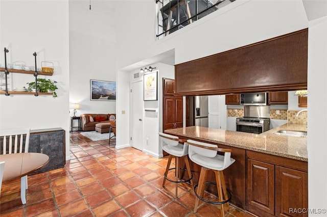 kitchen featuring stove, a breakfast bar, sink, a high ceiling, and stainless steel fridge