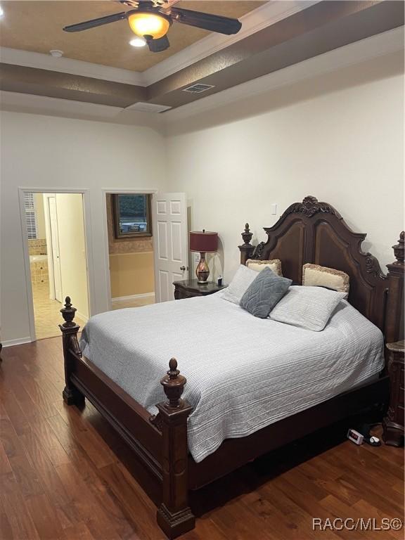 bedroom with ceiling fan, ensuite bathroom, a tray ceiling, ornamental molding, and dark hardwood / wood-style flooring