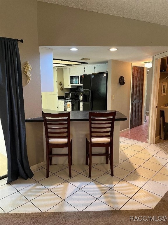 kitchen with kitchen peninsula, white cabinetry, light tile patterned floors, and black appliances