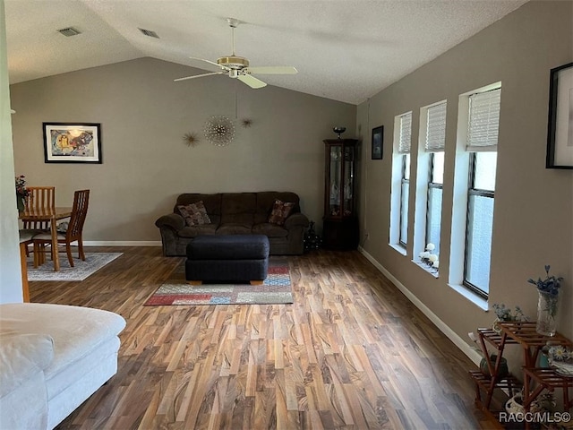 living room with a textured ceiling, ceiling fan, dark wood-type flooring, and vaulted ceiling