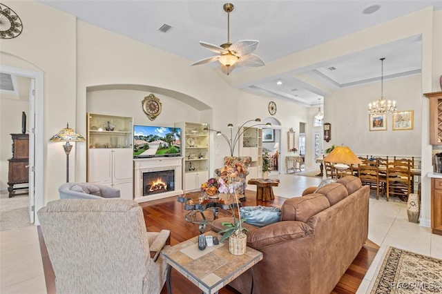 tiled living room with ceiling fan with notable chandelier and a raised ceiling