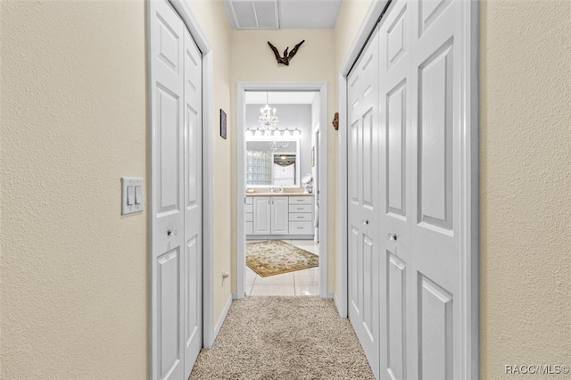 hallway featuring light carpet and a notable chandelier