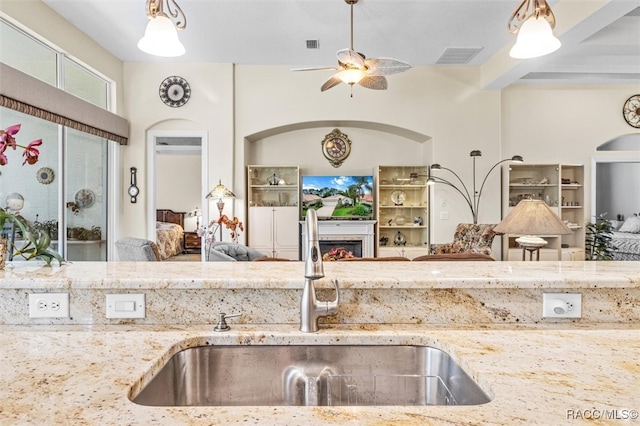 kitchen featuring beamed ceiling, ceiling fan, light stone countertops, and sink