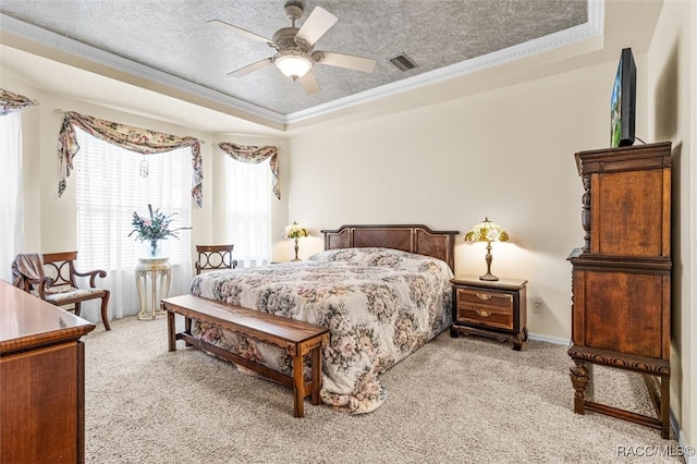 bedroom with a textured ceiling, a tray ceiling, light colored carpet, ceiling fan, and crown molding