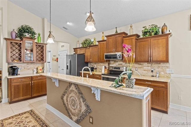 kitchen featuring hanging light fixtures, backsplash, an island with sink, vaulted ceiling, and appliances with stainless steel finishes