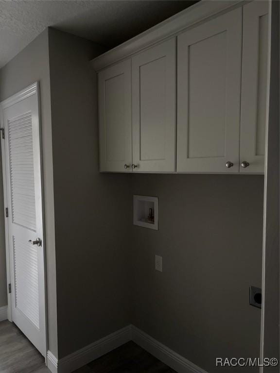 clothes washing area featuring hookup for a washing machine, cabinet space, a textured ceiling, wood finished floors, and baseboards