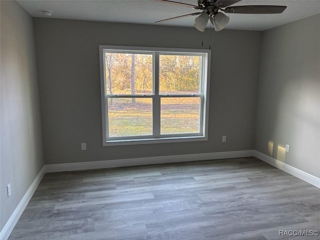 spare room featuring ceiling fan, light wood-type flooring, and baseboards