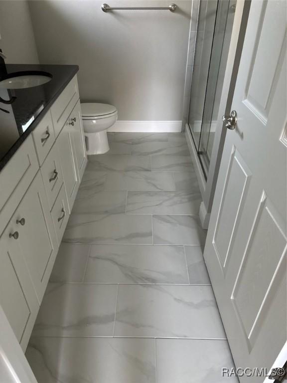 full bathroom featuring toilet, vanity, baseboards, marble finish floor, and a shower stall