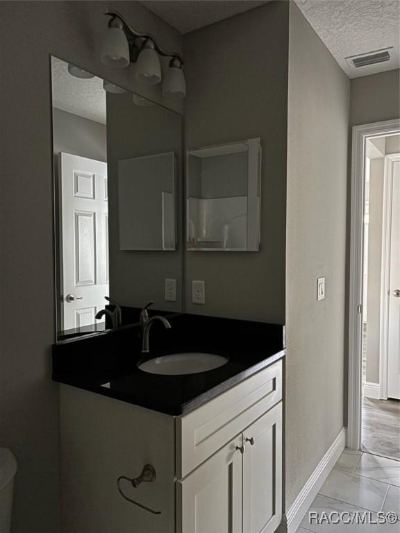 bathroom with baseboards, visible vents, a textured ceiling, and vanity