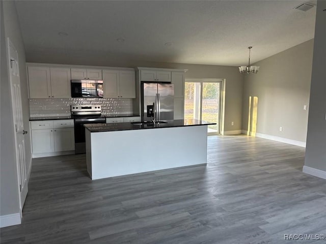 kitchen with dark countertops, visible vents, hanging light fixtures, appliances with stainless steel finishes, and a kitchen island with sink