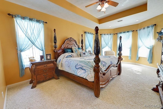 carpeted bedroom with multiple windows, a textured ceiling, a raised ceiling, and ceiling fan