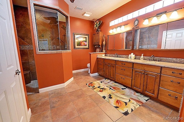 bathroom with a tile shower, tile patterned flooring, vanity, toilet, and a textured ceiling