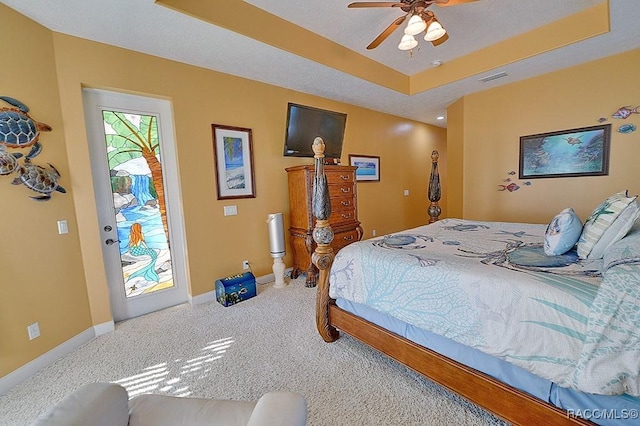 carpeted bedroom featuring ceiling fan, a tray ceiling, and access to exterior