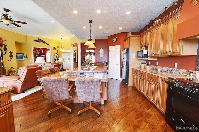 kitchen with light stone countertops, a kitchen island, black appliances, and a kitchen bar