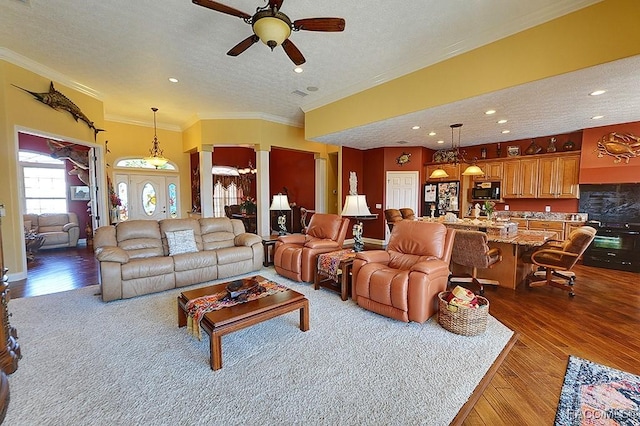 living room featuring ornamental molding, light wood-type flooring, a textured ceiling, and ornate columns