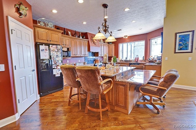 kitchen featuring a kitchen bar, light stone counters, wood-type flooring, a kitchen island, and black appliances