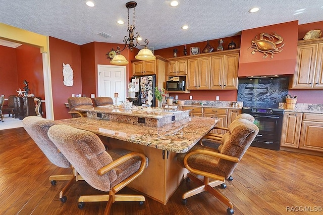 kitchen with light hardwood / wood-style floors, black appliances, a center island, and a kitchen bar