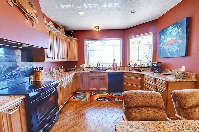 kitchen featuring sink, light stone counters, a textured ceiling, light hardwood / wood-style flooring, and black appliances