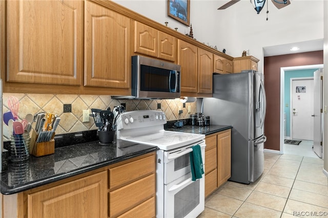 kitchen with backsplash, dark stone counters, stainless steel appliances, ceiling fan, and light tile patterned floors