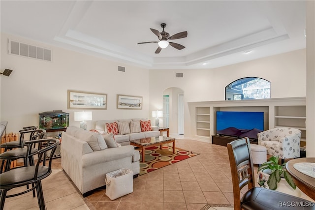 tiled living room featuring a high ceiling, a tray ceiling, built in features, and ceiling fan