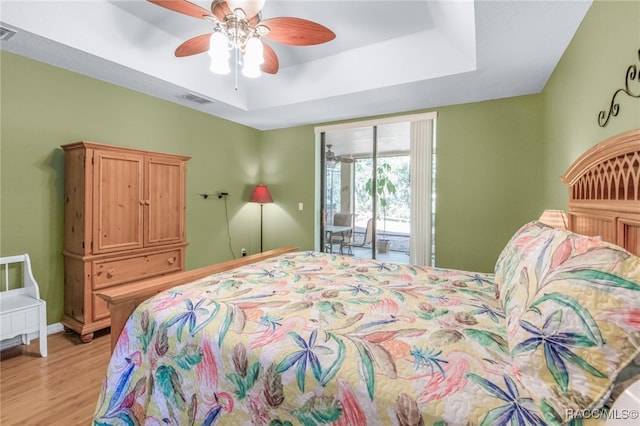 bedroom featuring access to outside, a raised ceiling, ceiling fan, and light hardwood / wood-style floors