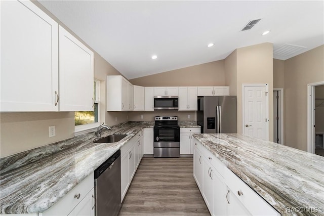 kitchen featuring stainless steel appliances, light stone countertops, vaulted ceiling, white cabinets, and sink