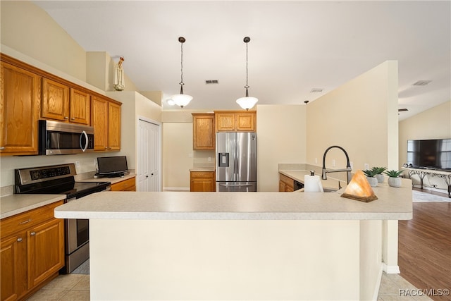 kitchen with a large island with sink, pendant lighting, stainless steel appliances, and light hardwood / wood-style floors