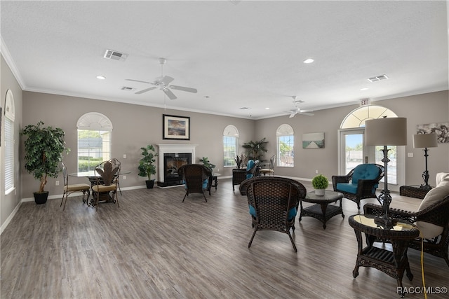 living room featuring dark wood-type flooring, crown molding, ceiling fan, and a healthy amount of sunlight