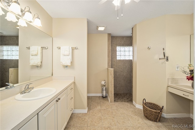 bathroom featuring vanity, a textured ceiling, ceiling fan, tiled shower, and tile patterned flooring