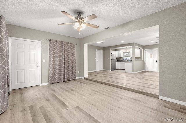 unfurnished living room with ceiling fan, a textured ceiling, and light wood-type flooring