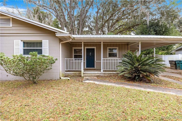 view of exterior entry with a carport, covered porch, and a lawn