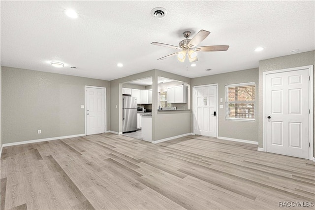 unfurnished living room featuring ceiling fan, light hardwood / wood-style floors, and a textured ceiling