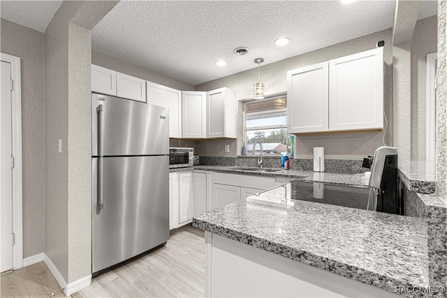 kitchen with white cabinets, sink, stainless steel fridge, a textured ceiling, and light stone counters